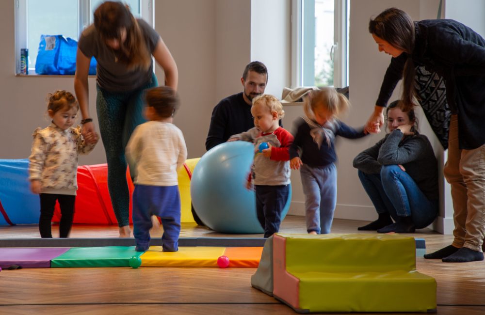 Un group d'enfants accompagné de leurs parents se déplacent sur des tapis lors d'un cours de gym.